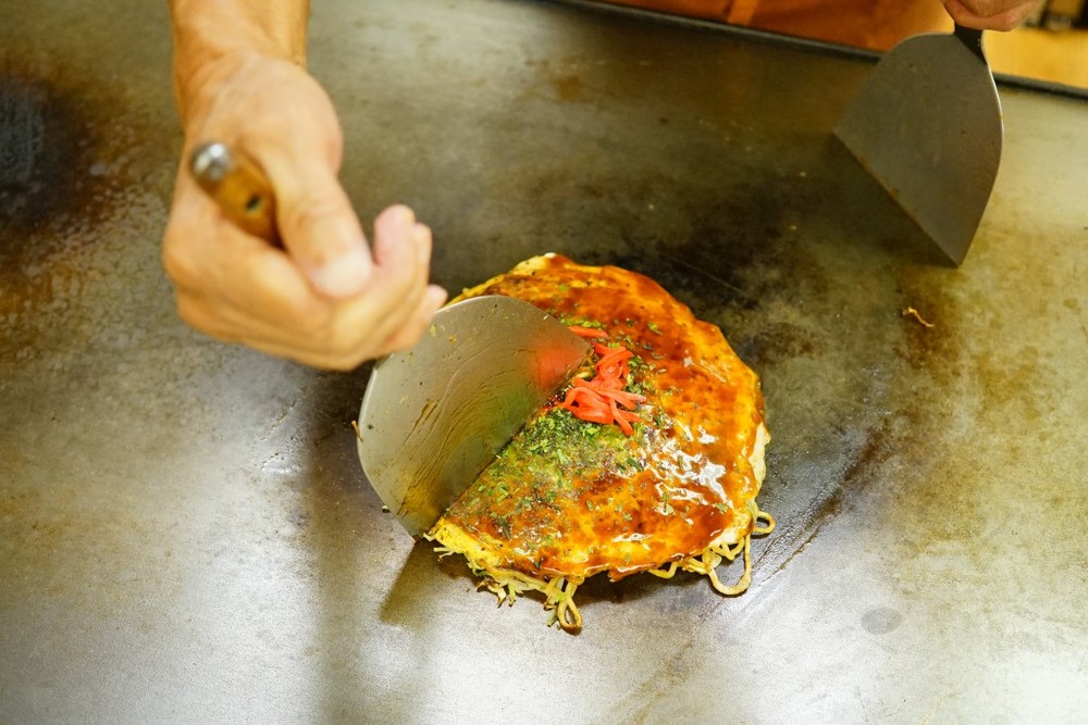 広島のお好み焼きは、薄めの生地にたっぷりと入った焼きそば、野菜が特徴。鉄板でご主人自ら焼いてくれる。