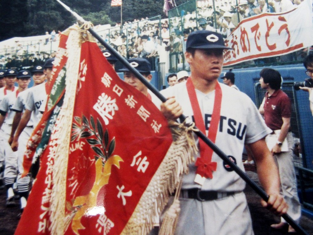 新潟県大会の優勝旗を手に球場を行進する主将・鈴木さんと中越高校チーム。